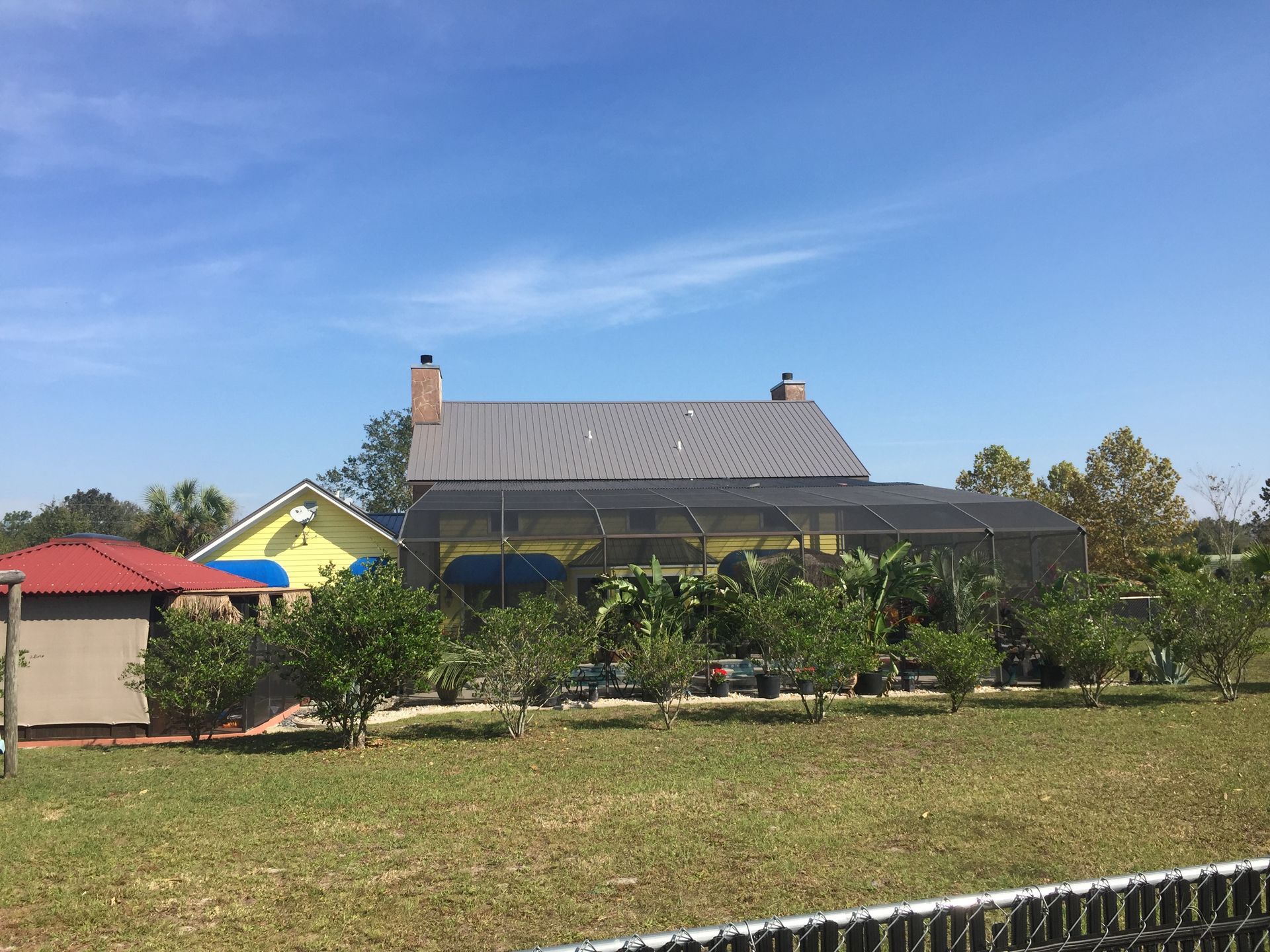 Single-story house with gray roof, green yard, and blue sky on a sunny day