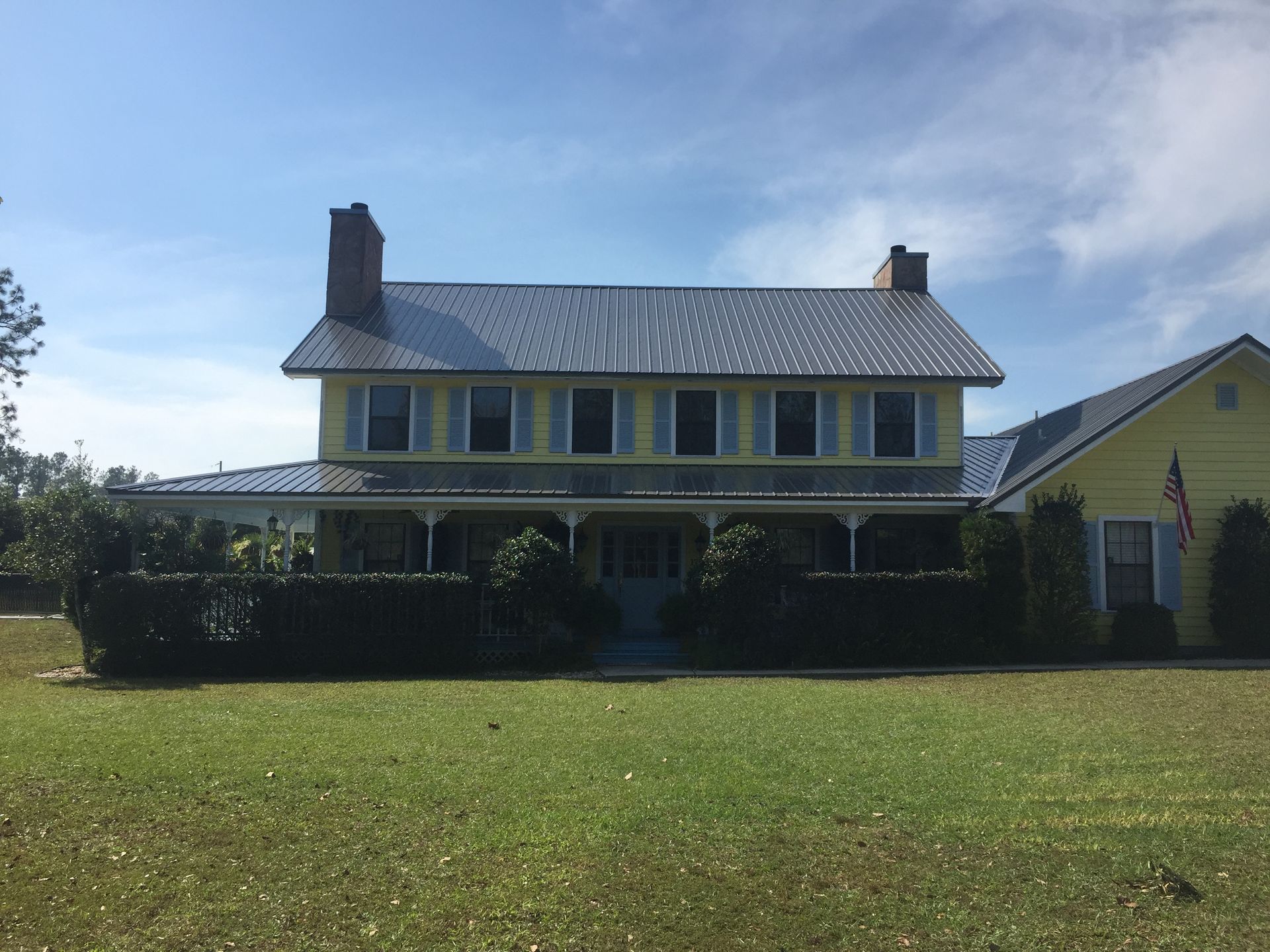 Yellow farmhouse with white trim and a long porch under a blue sky, viewed across a grassy lawn