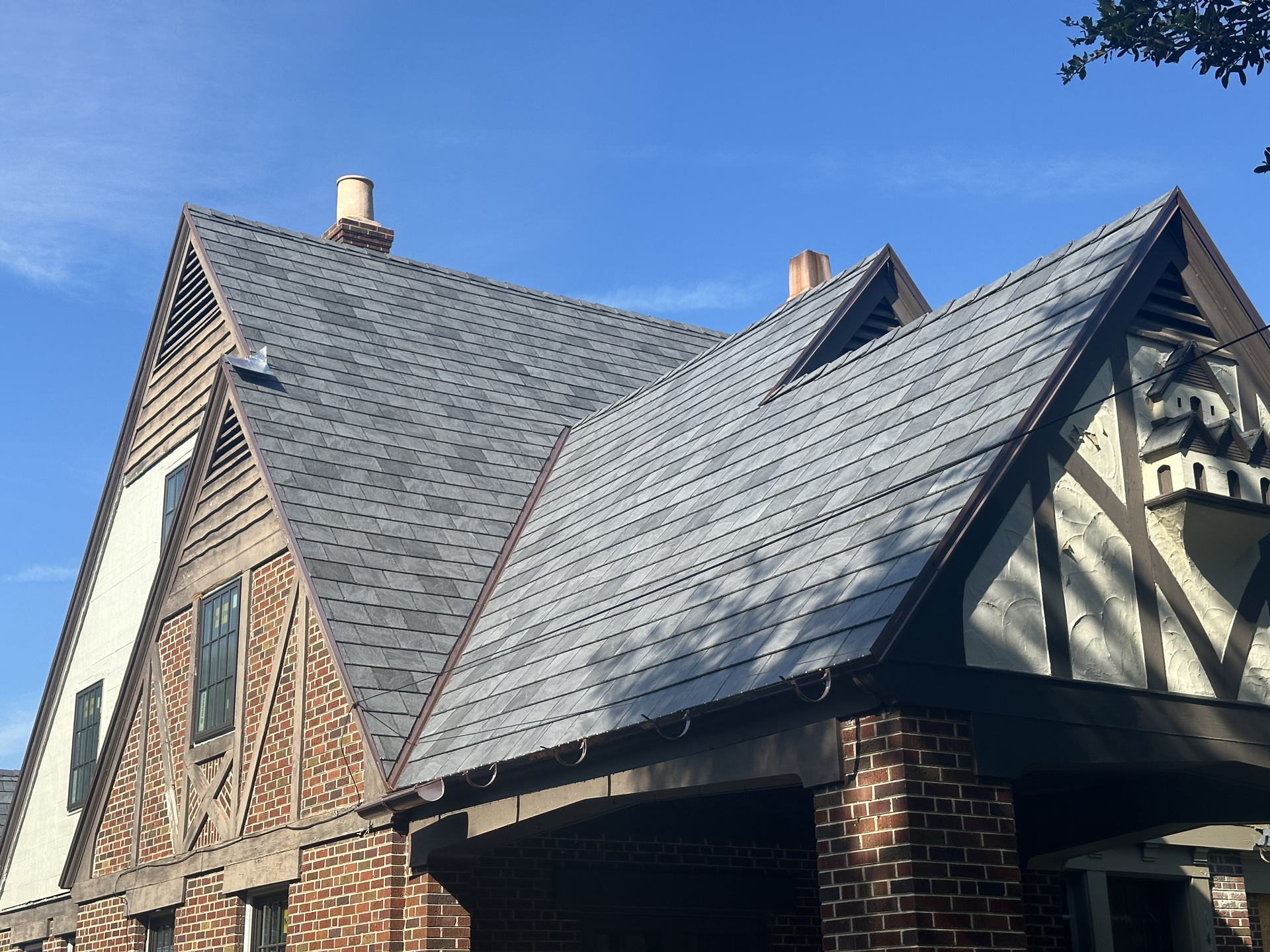 Brick house with steep gray shingle roof under a clear blue sky