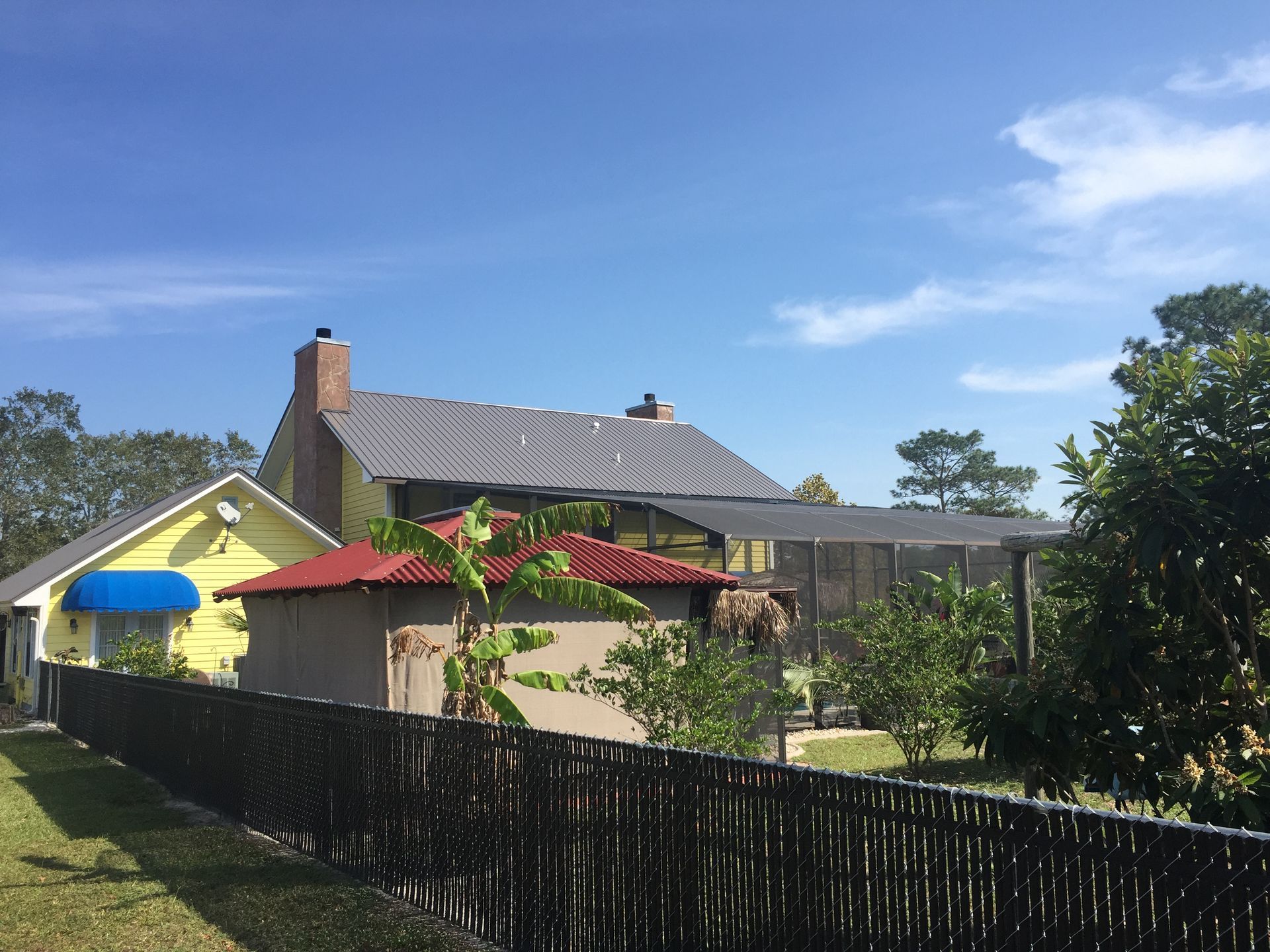 Residential backyard with yellow house, red roof, black fence, and blue sky