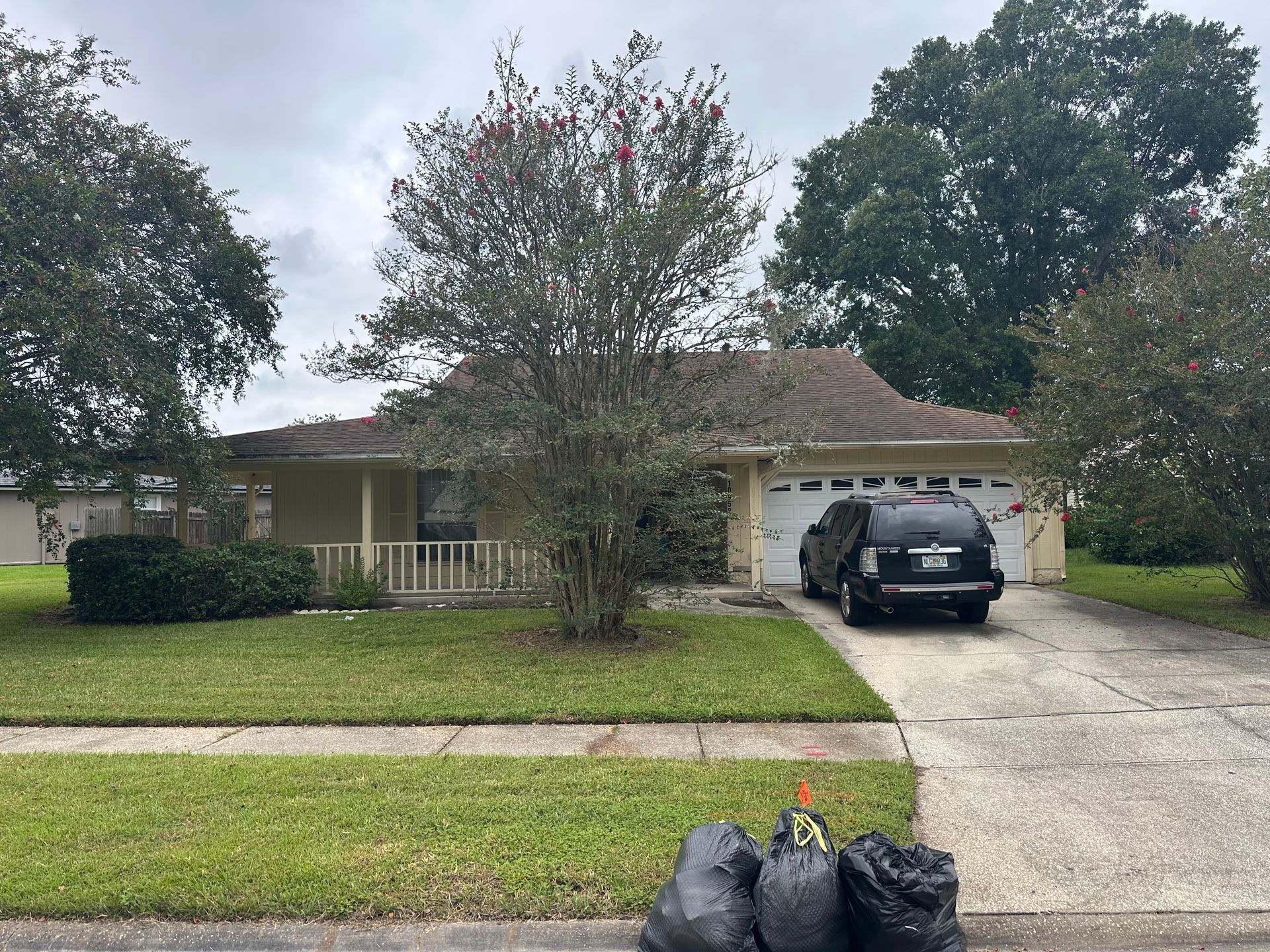 Suburban house with a front porch, lawn, driveway, and black SUV parked outside.