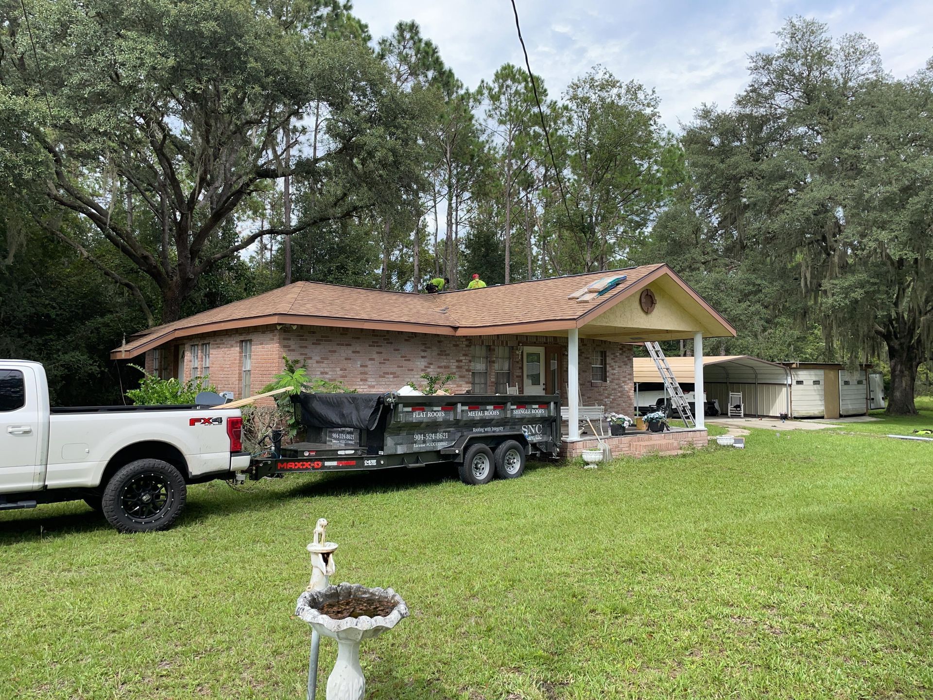 Truck and trailer parked beside a brick house with a new roof in a grassy yard