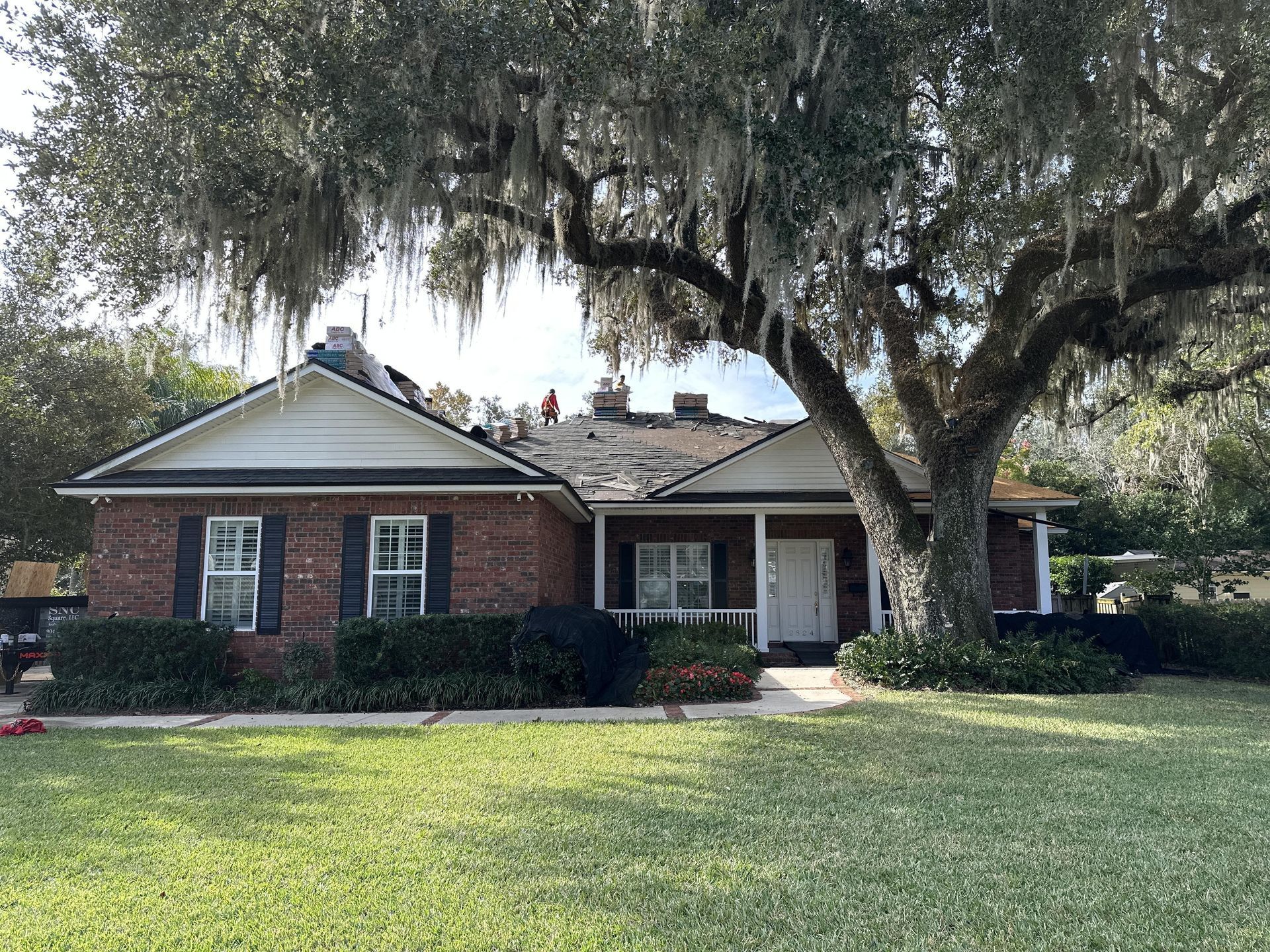 Brick suburban house with a large oak tree and green front lawn