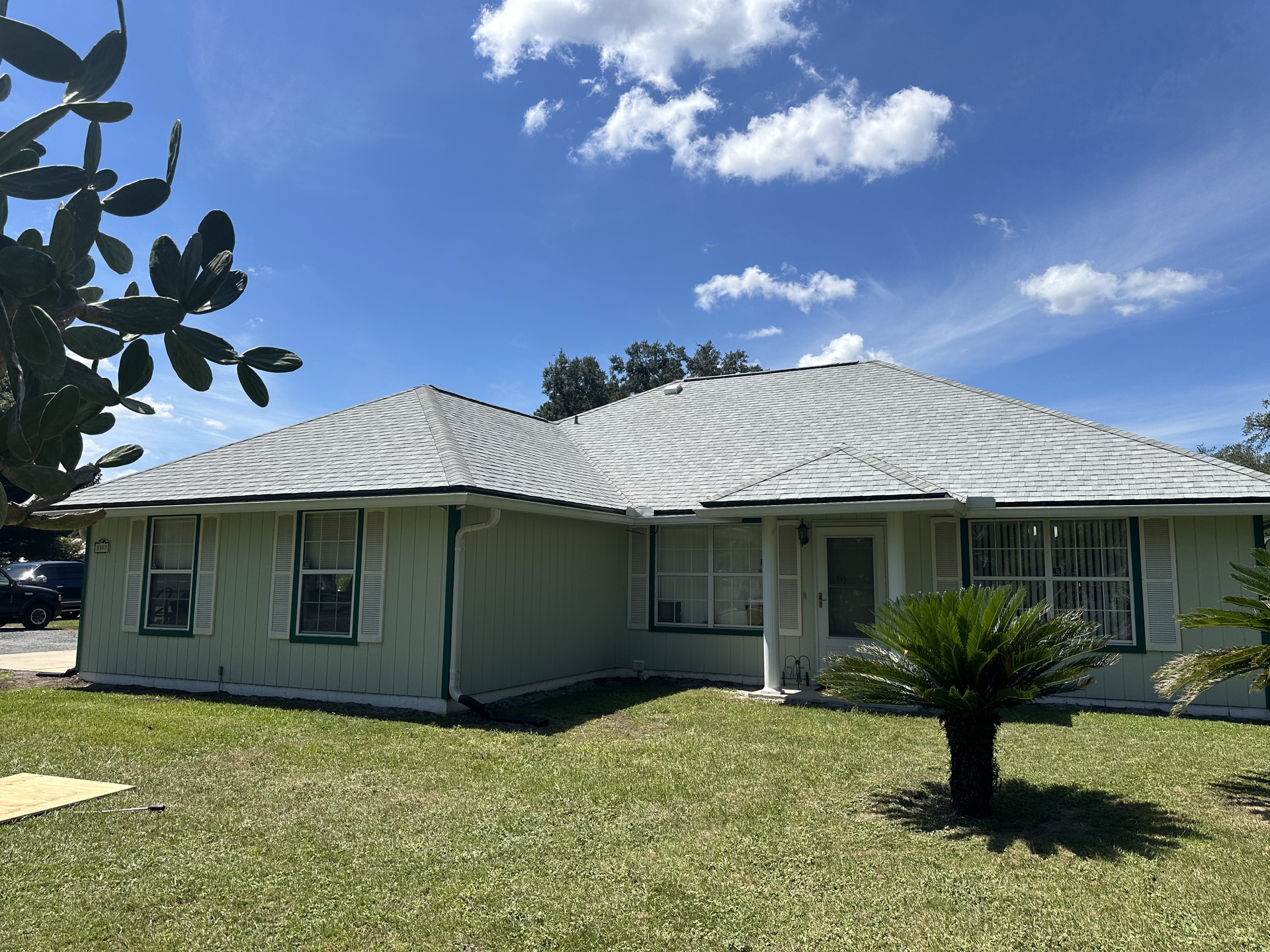 Single-story beige house with a white roof, green lawn, and blue sky with clouds