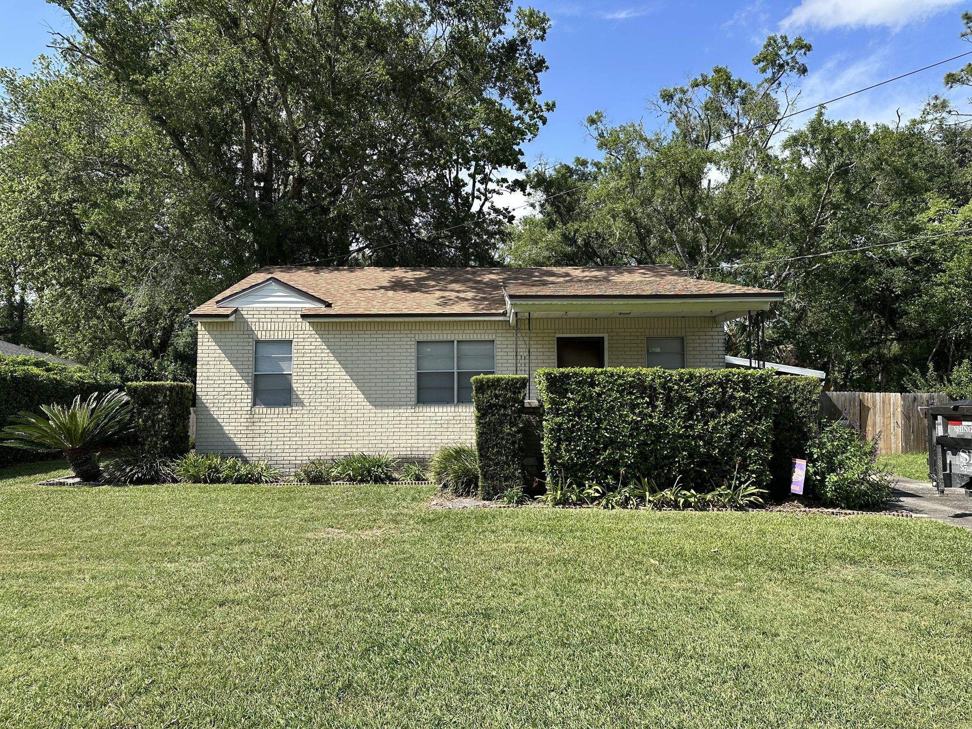 Small white house with a hedged front yard and large grassy lawn under trees
