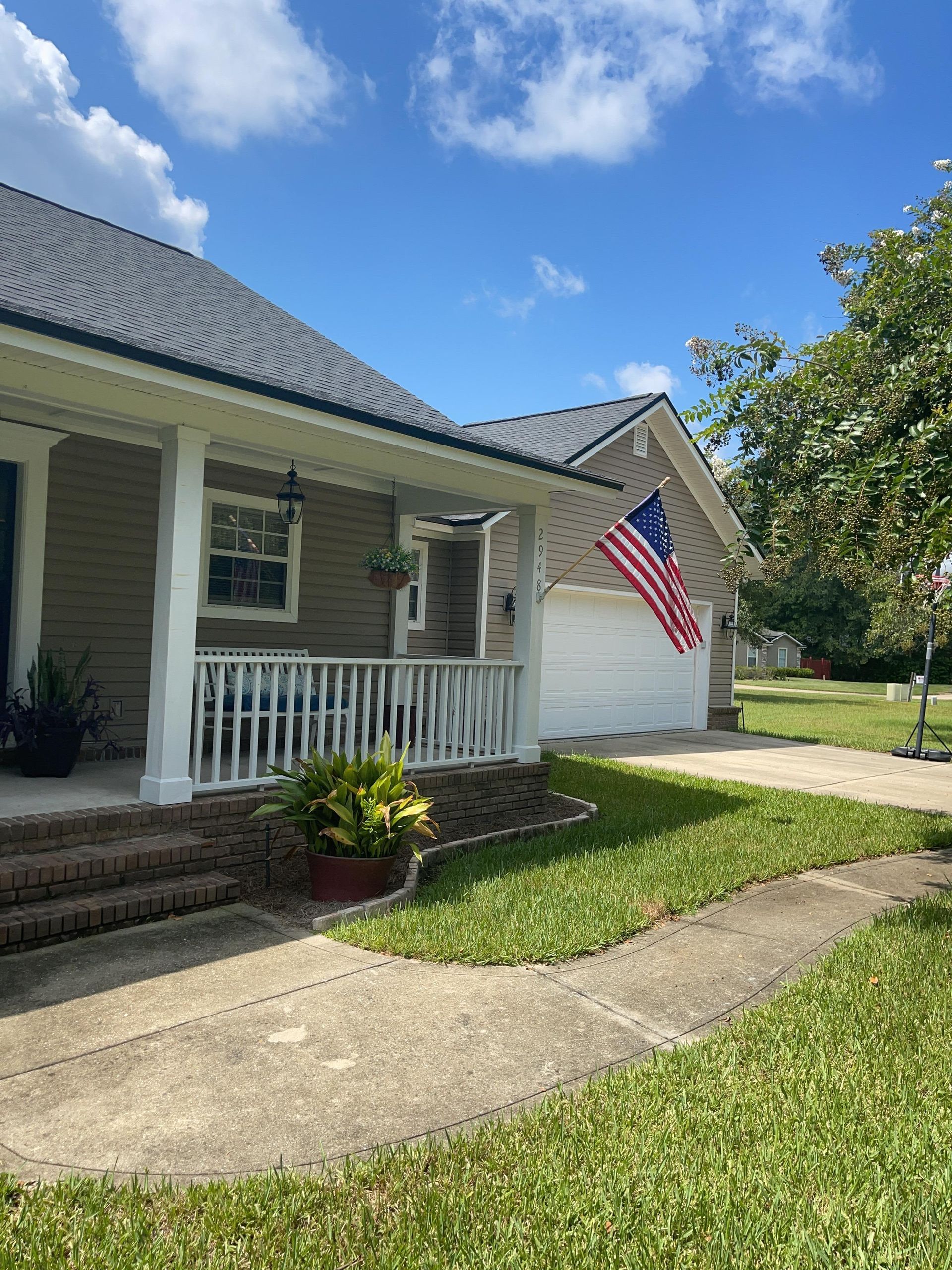 Front porch of a white house with an American flag, brick steps, and a sunlit lawn under a blue sky