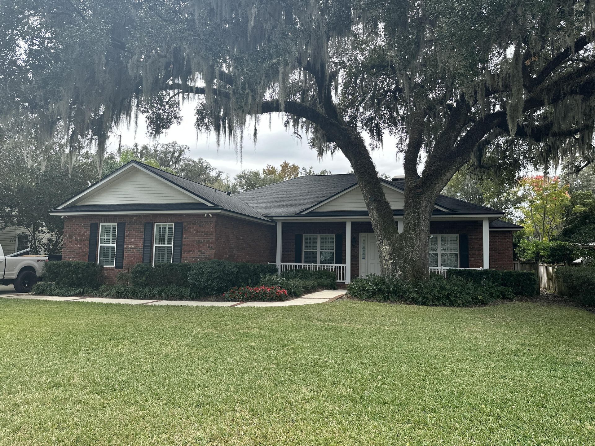 Single-story brick house with a large oak tree and front lawn in a quiet suburban neighborhood