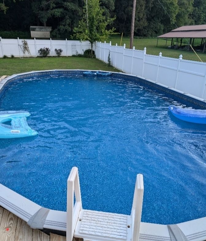 Backyard above-ground pool with blue water, white fence, and pool ladder in the foreground
