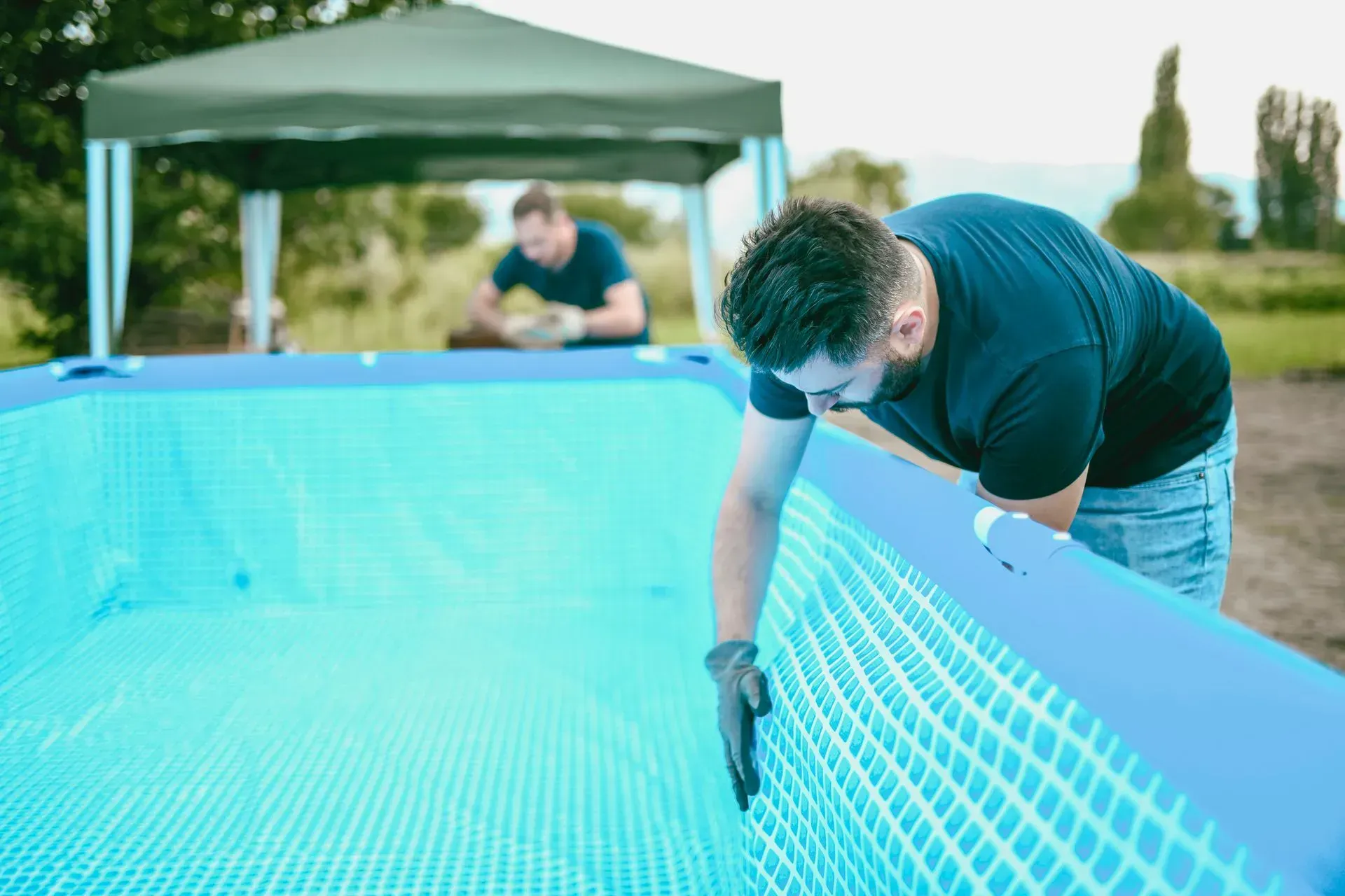 Person cleaning a blue above-ground pool beside a green canopy tent