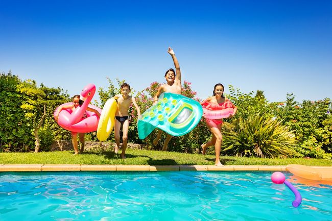 People posing by a pool with colorful inflatable letters and flamingos on a sunny day