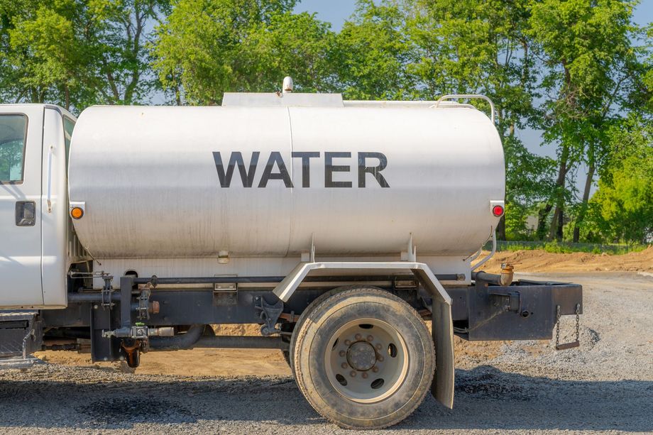White water tanker truck parked on gravel, with trees in the background.