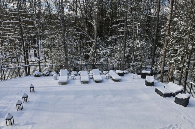 Snow-covered backyard deck with outdoor furniture surrounded by bare trees