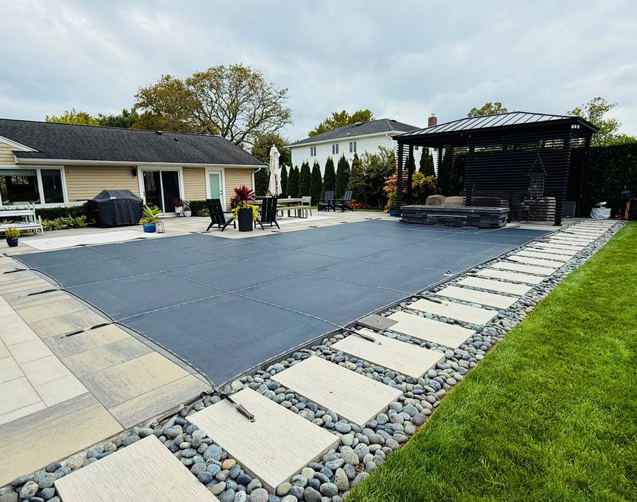 Backyard patio with a large gray trampoline, stone pavers, and a covered seating area.