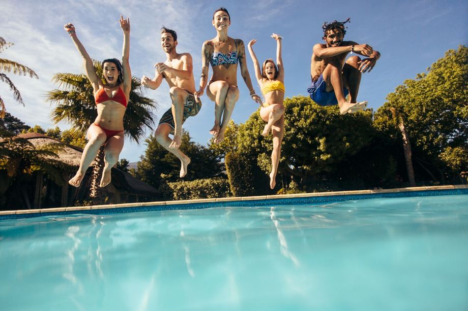 People jumping into a swimming pool on a sunny day