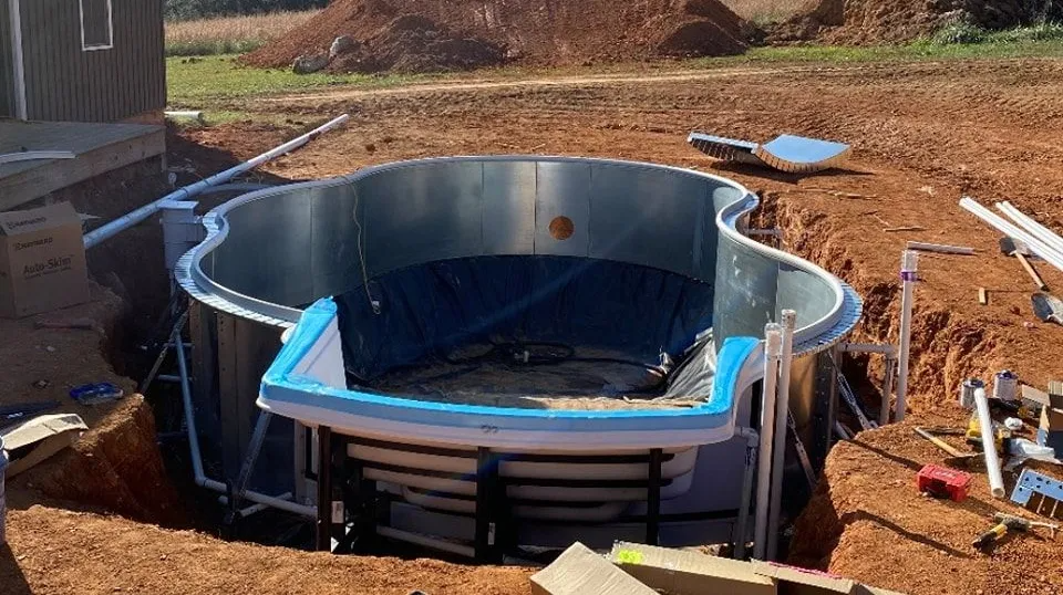 Partially built in-ground pool with blue liner and metal walls in a dirt backyard