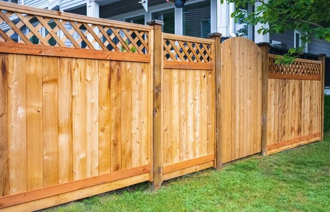 Wooden privacy fence with lattice top panels along a grassy yard beside a house.