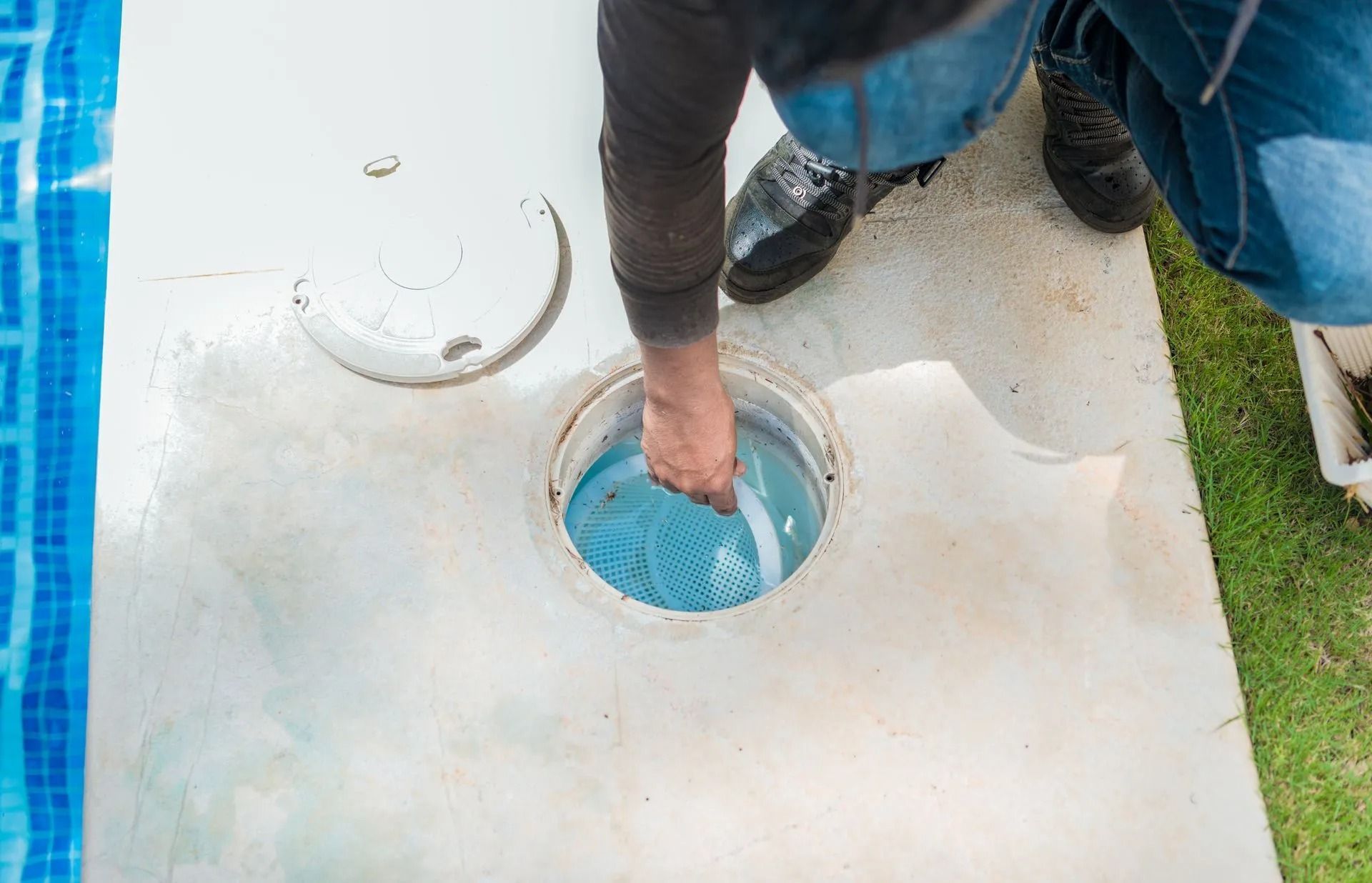 Person dipping a hand into a blue circular basin set in a concrete slab outdoors.