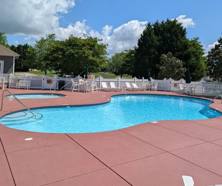 Outdoor swimming pool with blue water, red deck, lounge chairs, and umbrellas under a sunny sky
