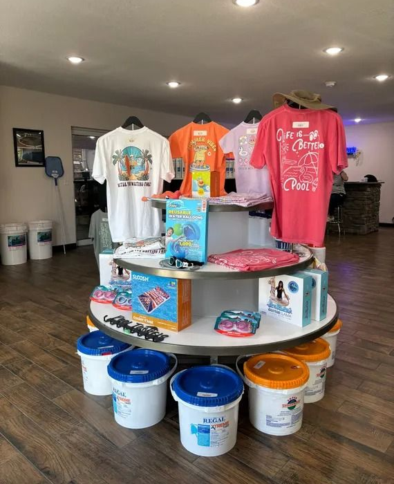 T-shirt display on a round table with paint buckets below in a store or workshop.