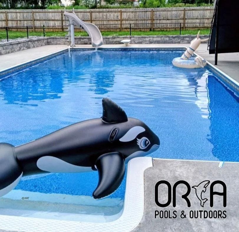 Black and white inflatable orca toys floating in a blue pool with an ORCA Pools & Outdoors sign