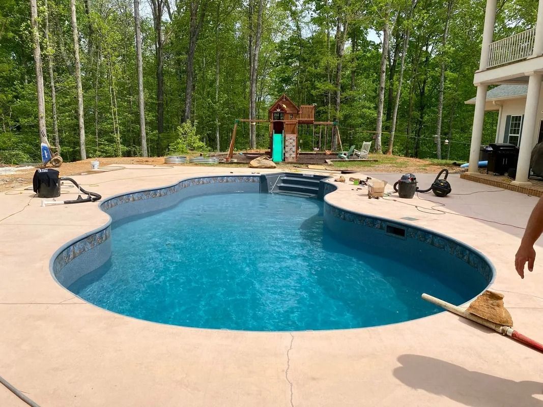 Backyard pool with blue water, tan deck, and wooded yard surrounding it