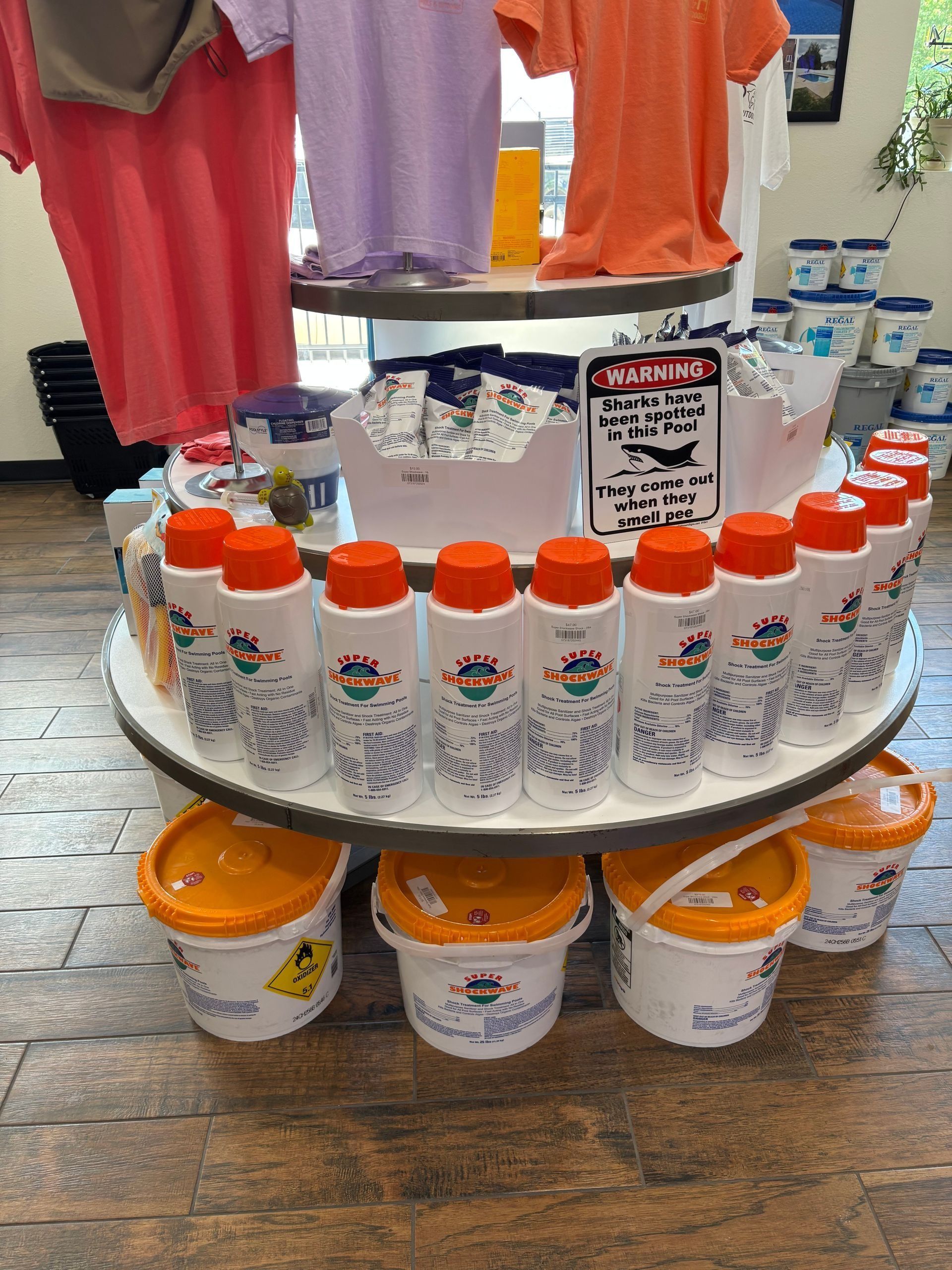 Colorful T-shirts hanging above display of orange-capped bottles and buckets on a table