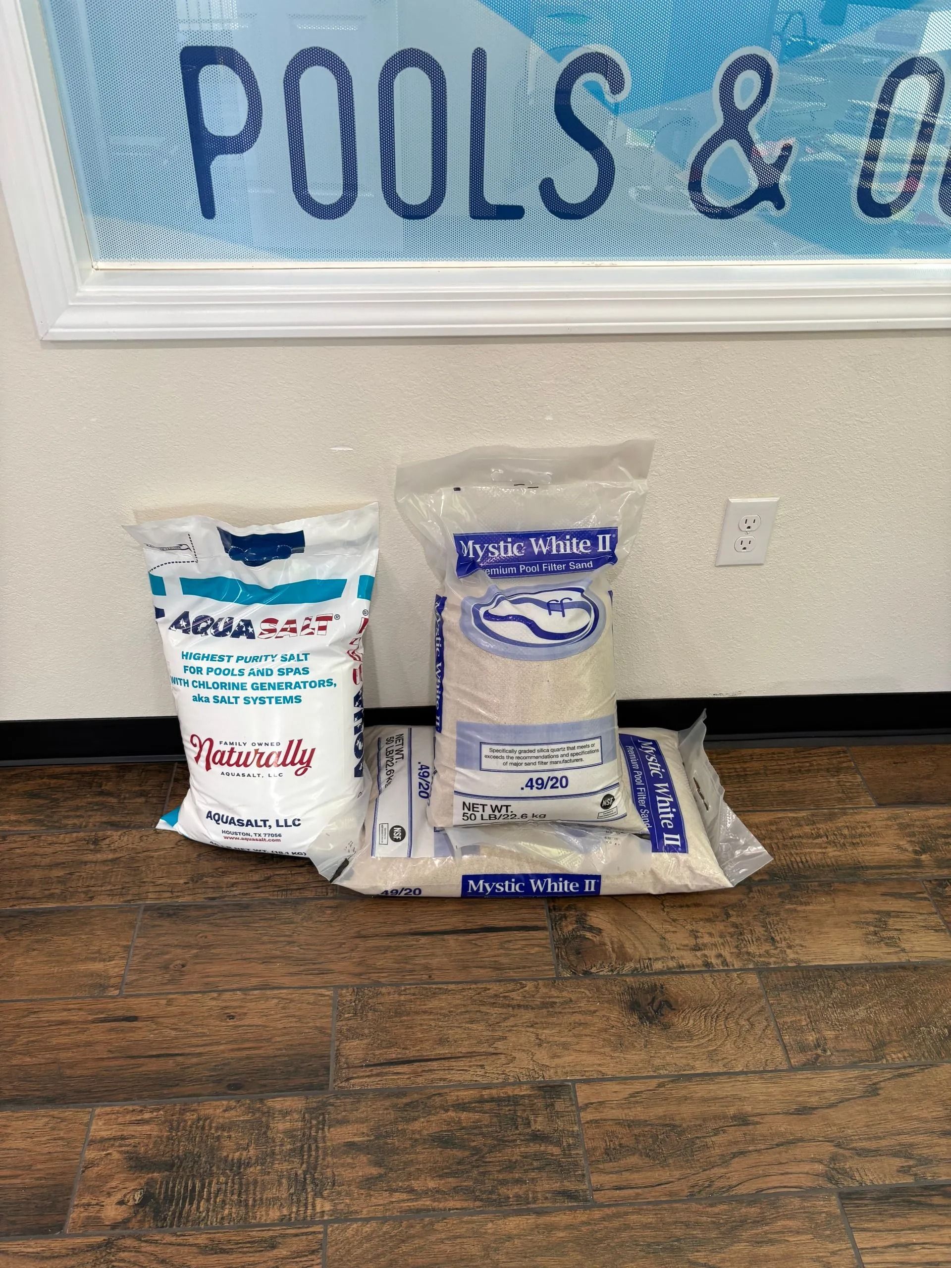 Two bags and a container of pool chemicals on a floor beneath a