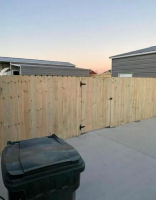 Wooden fence between two homes at sunset, with a black trash bin in the foreground.