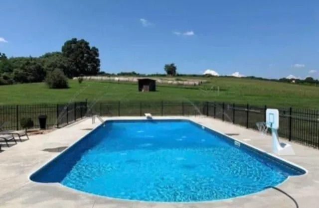 Outdoor swimming pool with blue water, fenced deck, and grassy hillside under a clear sky