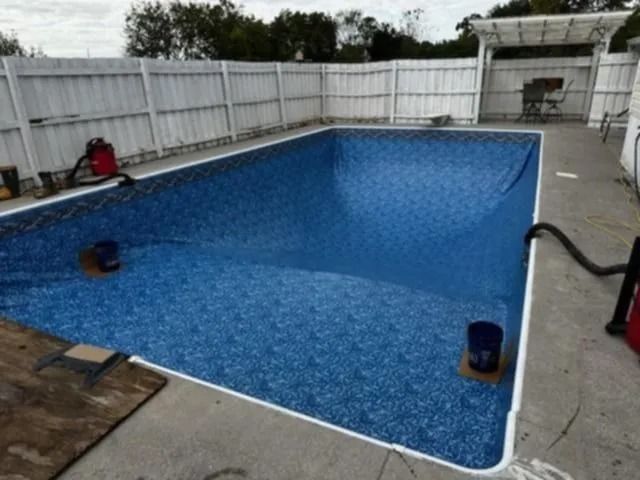 Empty blue backyard swimming pool with white fence and concrete deck