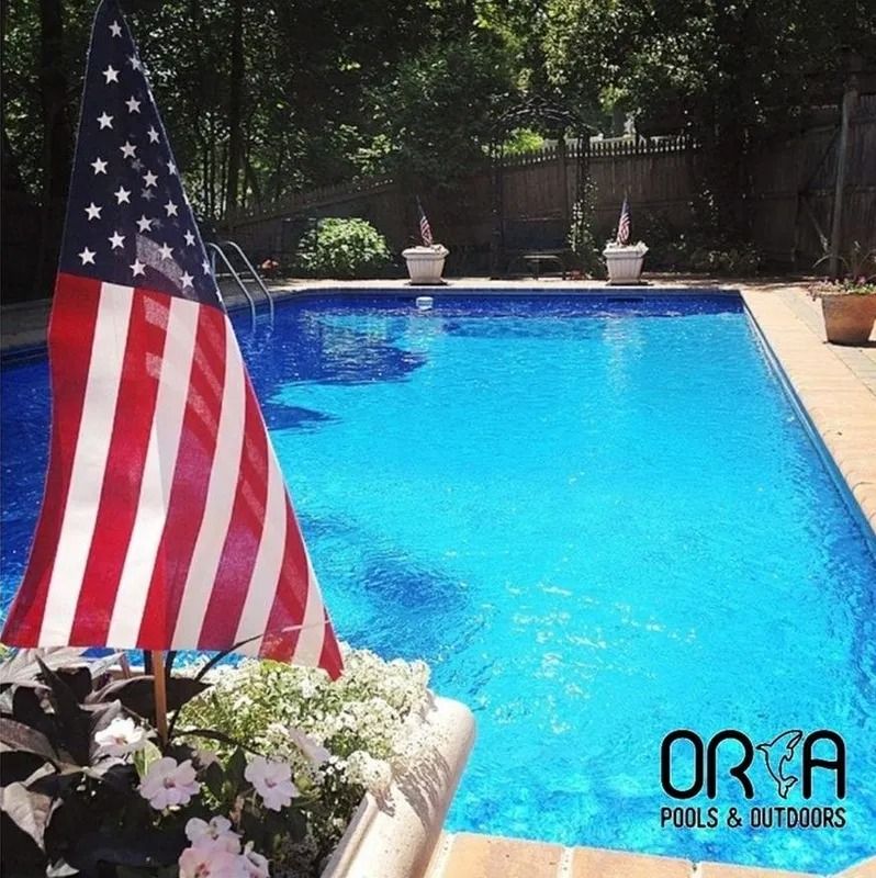American flag by a blue backyard swimming pool with flowers in the foreground