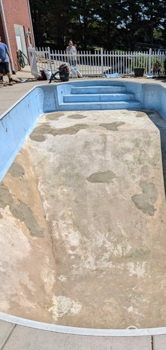 Empty backyard swimming pool with cracked concrete floor, blue walls, and steps at the shallow end