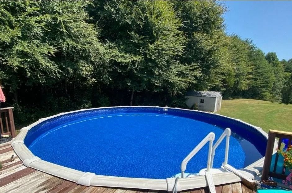 Round above-ground pool with blue cover in a wooded backyard under a clear sky