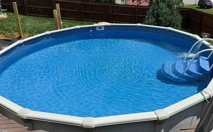 Above-ground backyard pool with blue water and a white ladder on a sunny day