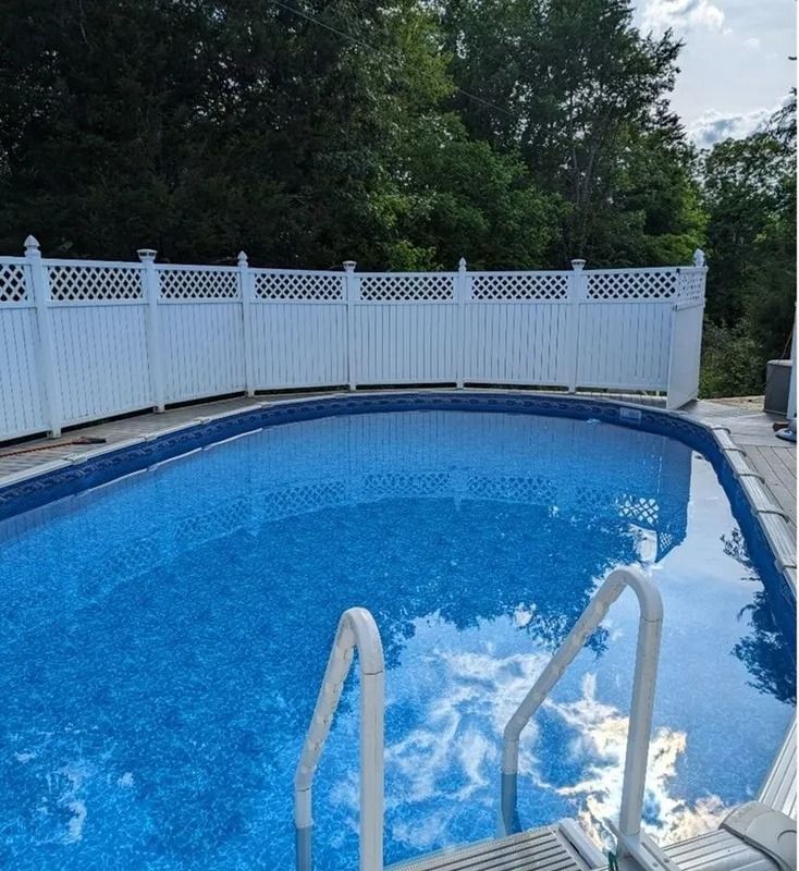 Backyard swimming pool with blue water, metal ladder, and white vinyl fence.