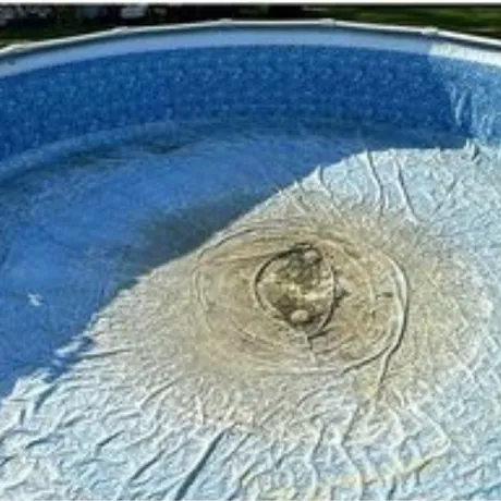 Blue swimming pool with a wrinkled pool liner bulging into a raised dome in the center