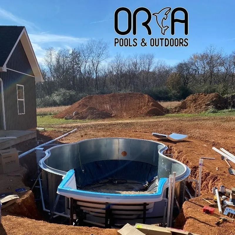 Round pool being installed beside a house at a dirt construction site, with ORCA Pools & Outdoors logo.