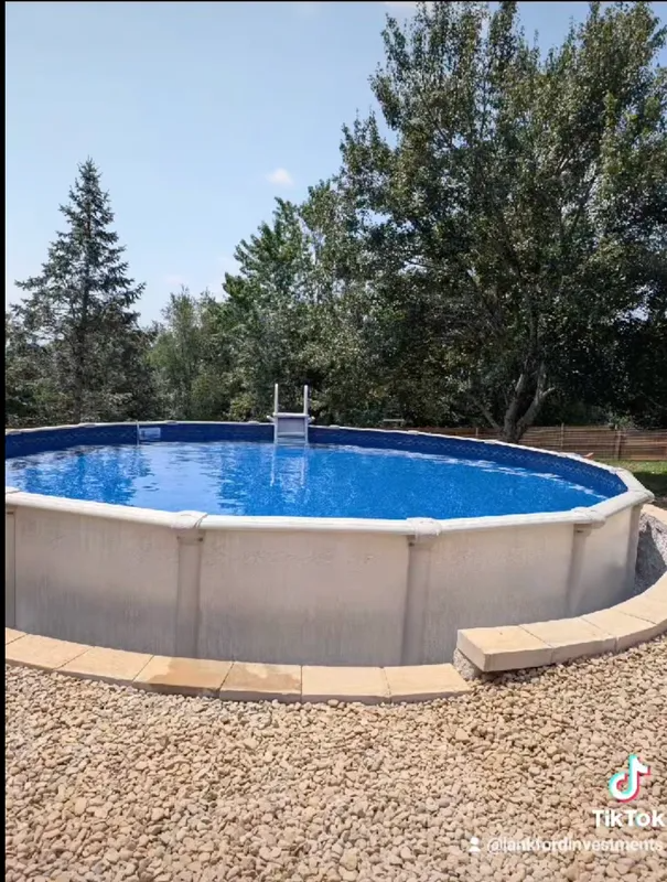 Above-ground backyard pool with blue water, surrounded by gravel and trees under a clear sky