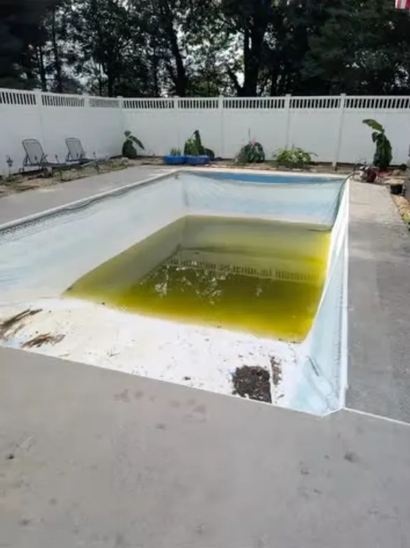 Empty drained swimming pool with yellow-green water and white walls outdoors