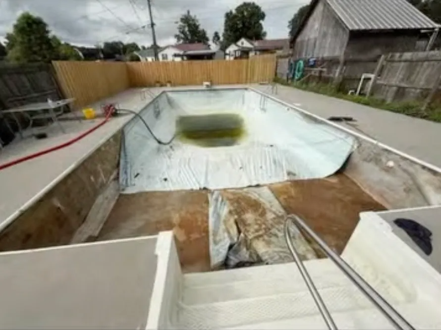 Empty in-ground pool under renovation with white liner and debris in a backyard.