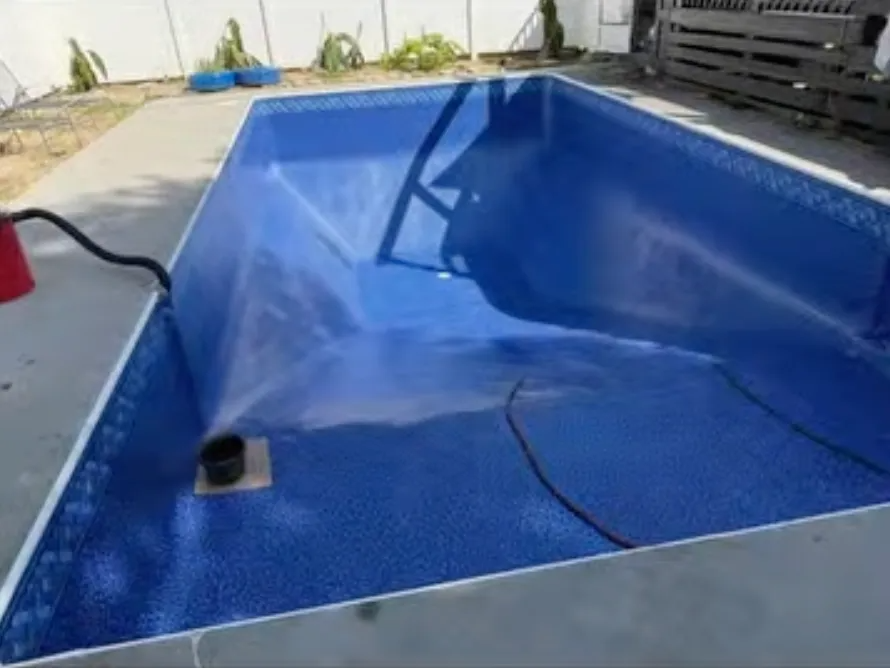 Empty blue swimming pool with a torn liner and a black hose inside, in a sunny outdoor yard