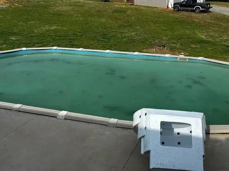 Covered swimming pool with green water beside a concrete deck and grassy yard.