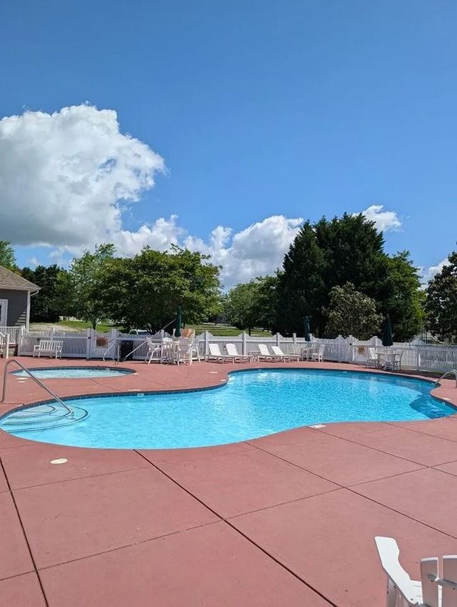 Backyard swimming pool with red deck, blue water, white lounge chairs, and cloudy blue sky