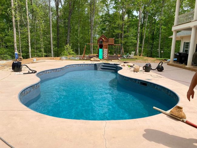 Backyard swimming pool with blue water, patio chairs, and trees surrounding it