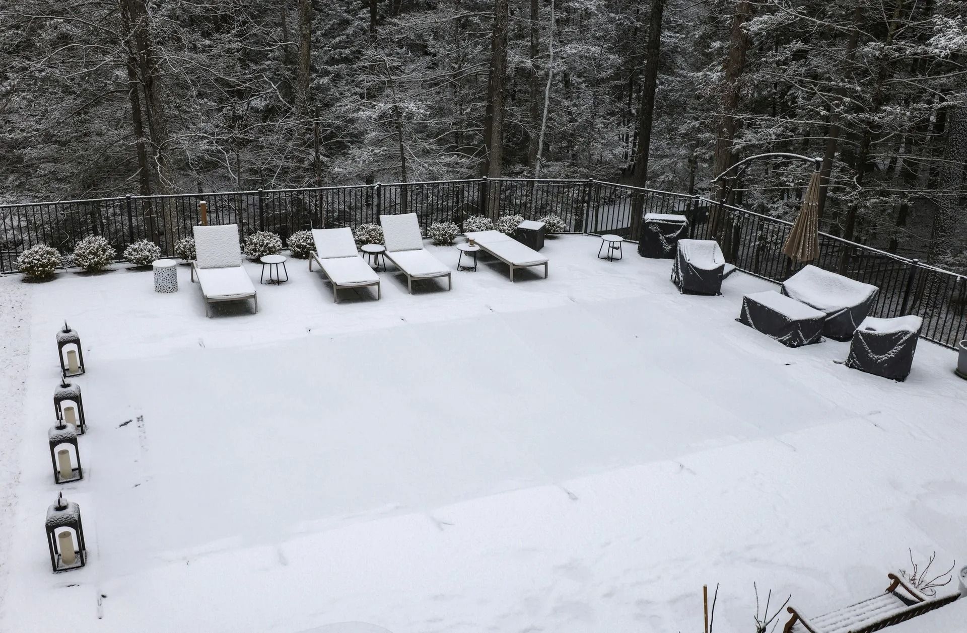 Snow-covered backyard with patio furniture and trees in winter.
