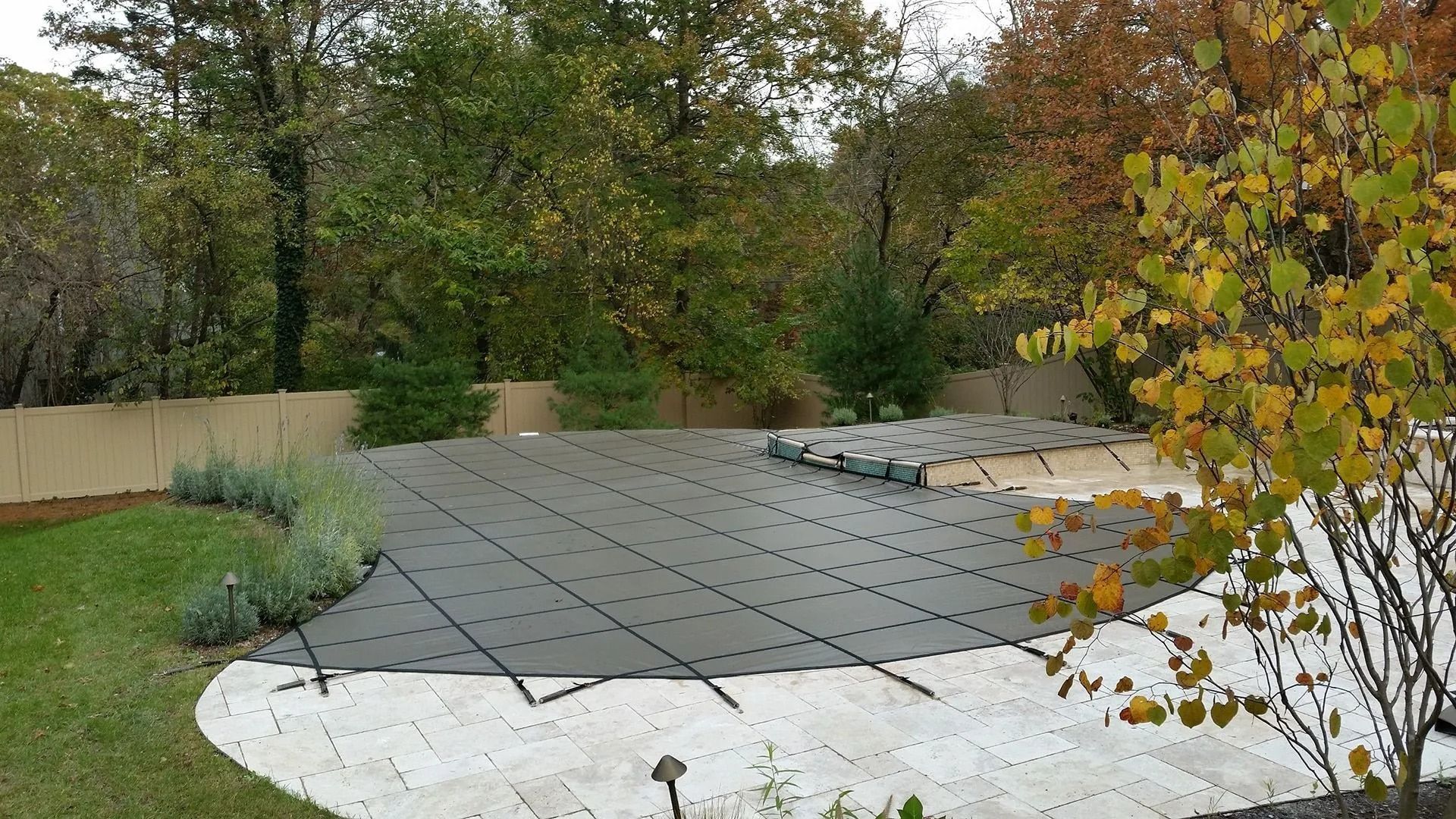 Covered patio under construction with dark pavers, white sand edges, and trees in the background