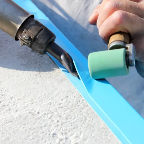 Person painting a blue edge with a roller brush over white textured surface