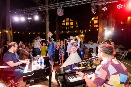 Bride and groom dance at a lively wedding reception with live musicians under stage lights.