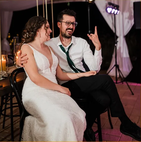 Smiling couple seated at a formal event, laughing together under purple stage lighting.