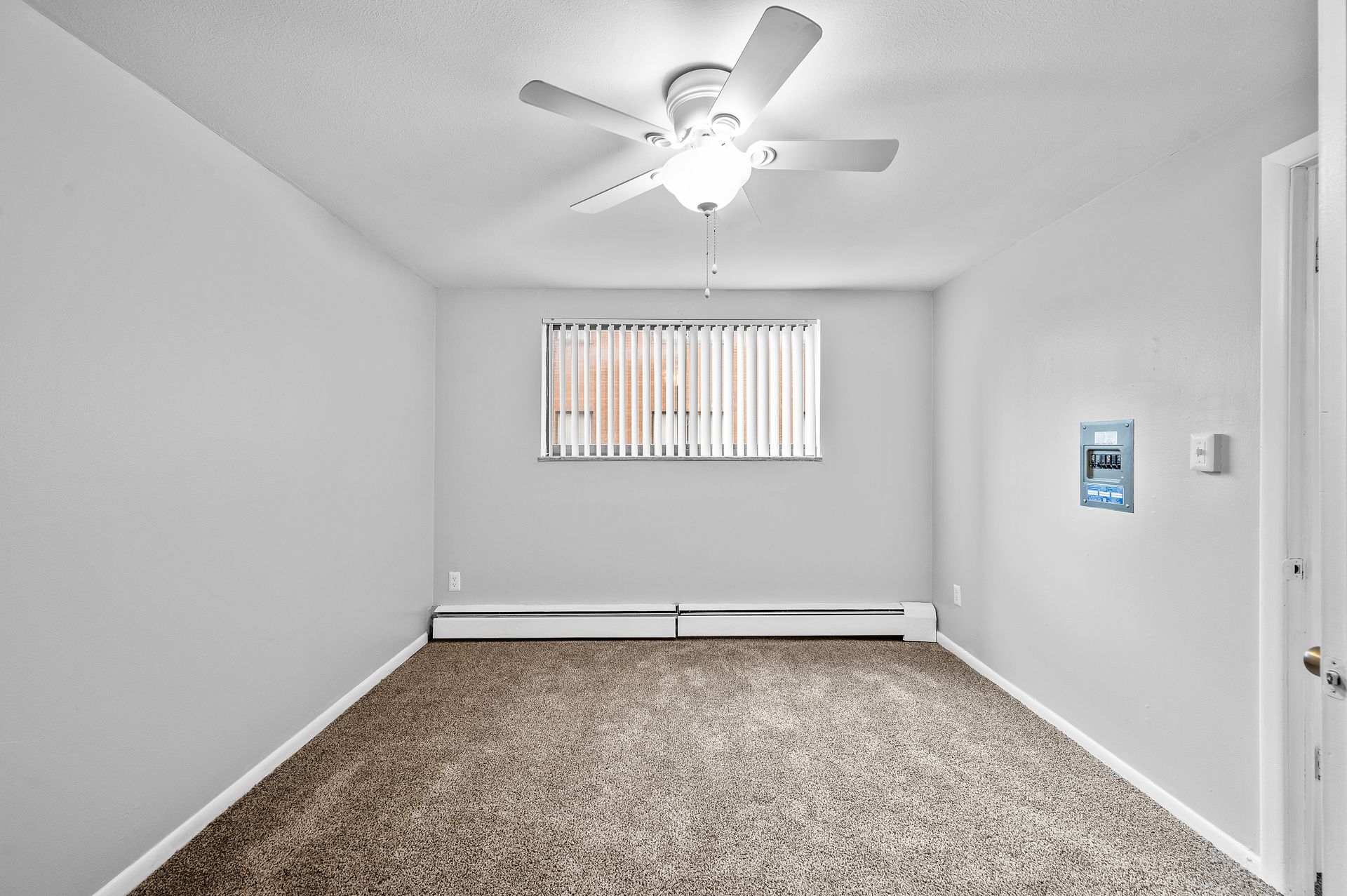 Empty room with gray walls, carpet, and a ceiling fan. Window with blinds. Electrical box on wall.